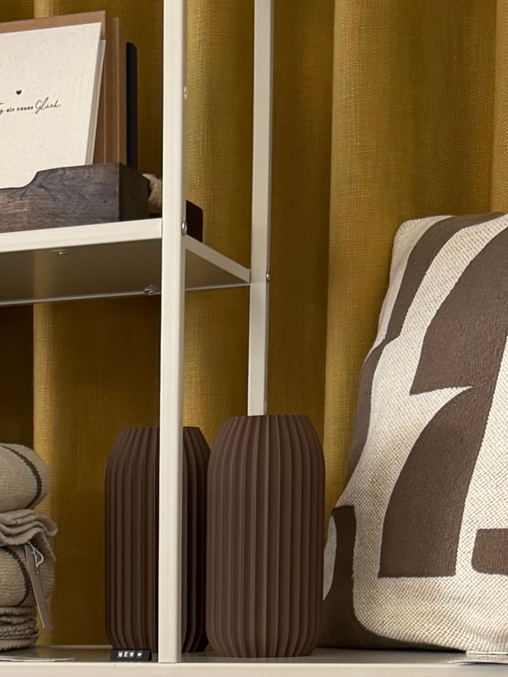 Zwei Vasen ELIN in Dark Chocolate in einem Regal neben einer gemusterten Decke